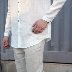 Pu&ograve; includere: Una camicia bianca di lino con colletto abbottonato e una tasca sul petto. La camicia &egrave; a maniche lunghe e ha una vestibilit&agrave; rilassata. Il modello indossa la camicia con pantaloni bianchi di lino.