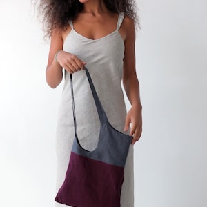 May include: A woman wearing a light grey linen dress holds a two-toned tote bag. The bag is made of a dark grey fabric on the top half and a burgundy fabric on the bottom half.