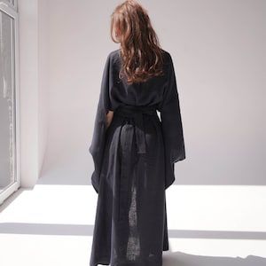 May include: A long, black linen robe with a wide, self-tie belt. The robe has long, wide sleeves and a flowing silhouette.