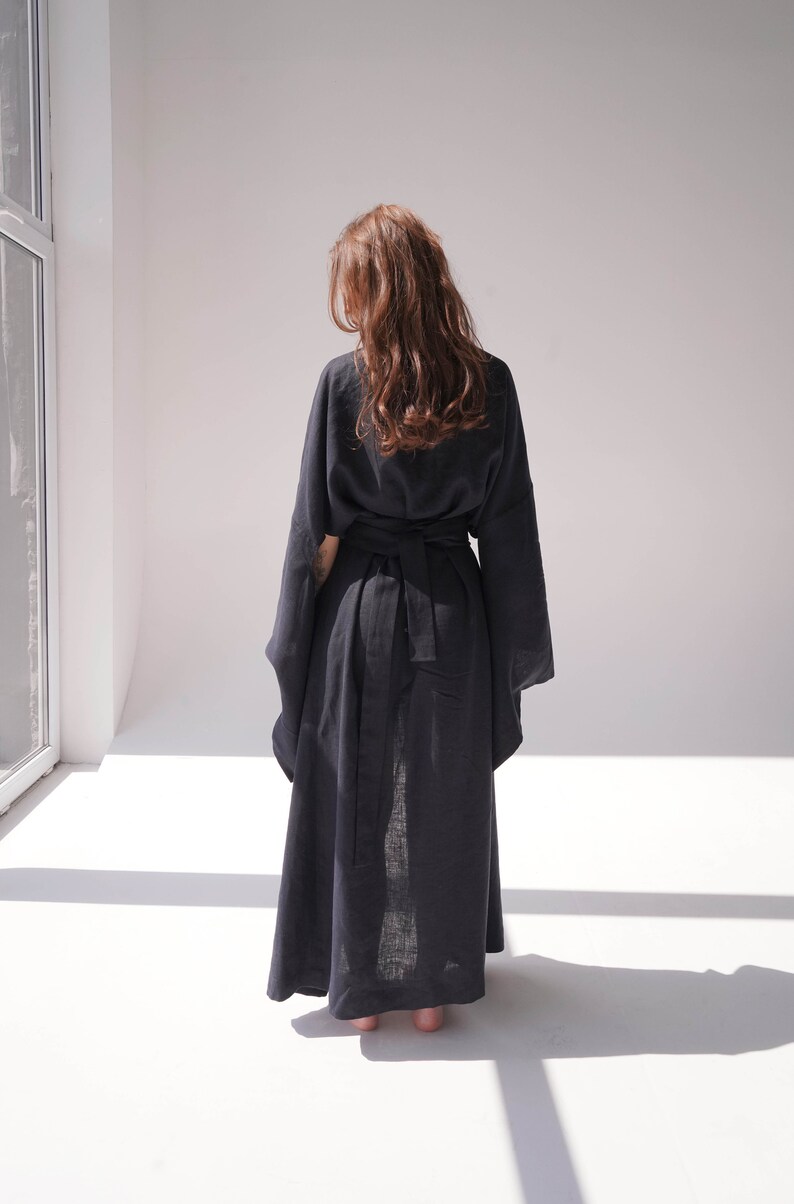 May include: A long, black linen robe with a wide, self-tie belt. The robe has long, wide sleeves and a flowing silhouette.