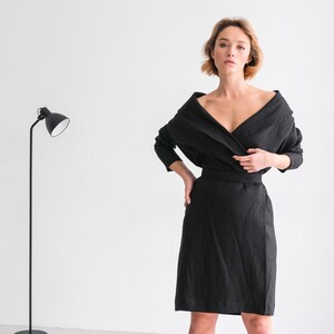 May include: A woman wearing a black linen wrap dress with a long sleeve and a V-neckline.