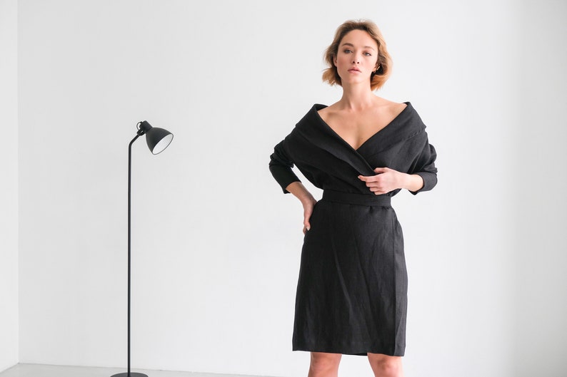 May include: A woman wearing a black linen wrap dress with a long sleeve and a V-neckline.