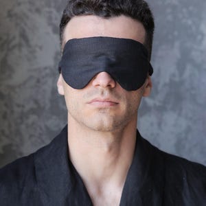 K&ouml;nnte beinhalten: Eine Person tr&auml;gt eine schwarze Schlafmaske und einen schwarzen Bademantel.