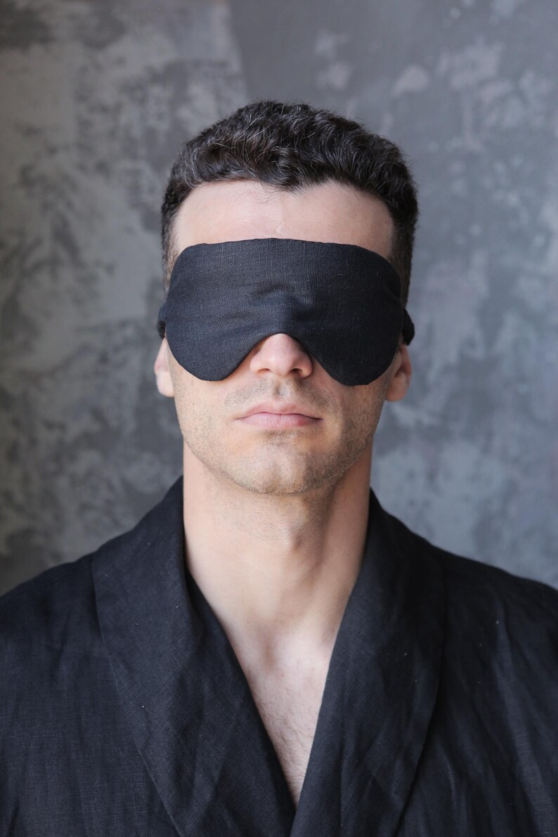 K&ouml;nnte beinhalten: Eine Person tr&auml;gt eine schwarze Schlafmaske und einen schwarzen Bademantel.