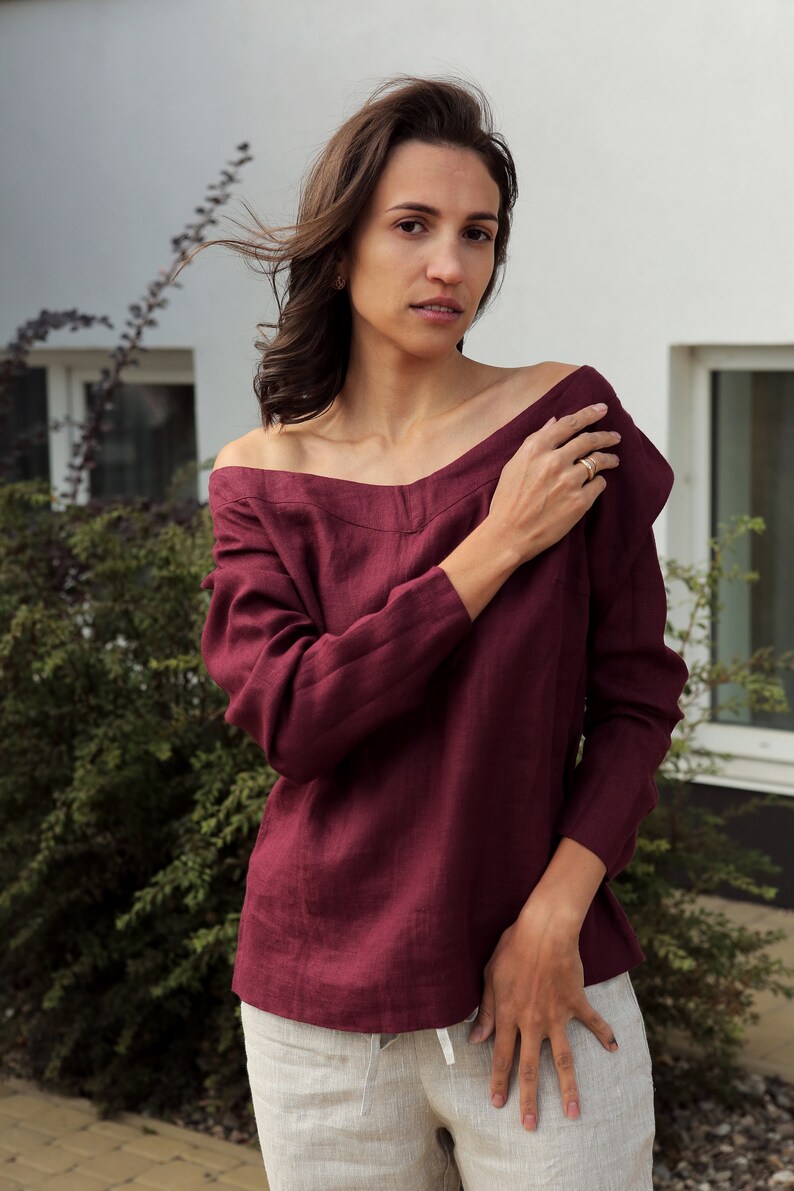 May include: A burgundy off-the-shoulder linen top with long sleeves. The top is made of a soft, lightweight fabric and has a relaxed fit.