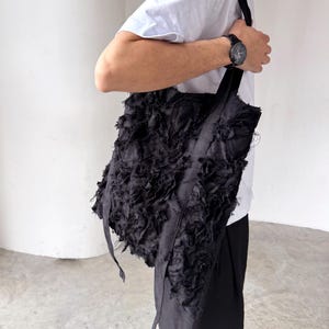 Peut inclure: Sac fourre-tout noir avec un design en tissu textur&eacute; et d&eacute;chiquet&eacute;. Le sac a de longues sangles et une forme rectangulaire. Le sac est port&eacute; &agrave; l'&eacute;paule. Le sac est fait d'un mat&eacute;riau sombre.