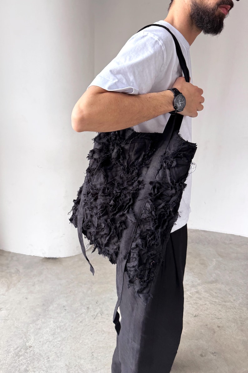 Peut inclure: Sac fourre-tout noir avec un design en tissu textur&eacute; et d&eacute;chiquet&eacute;. Le sac a de longues sangles et une forme rectangulaire. Le sac est port&eacute; &agrave; l'&eacute;paule. Le sac est fait d'un mat&eacute;riau sombre.