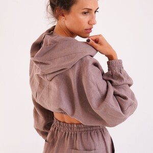 May include: A mauve linen hooded jumpsuit with a cropped top and long pants. The top has a drawstring waist and the pants have a patch pocket on the back.