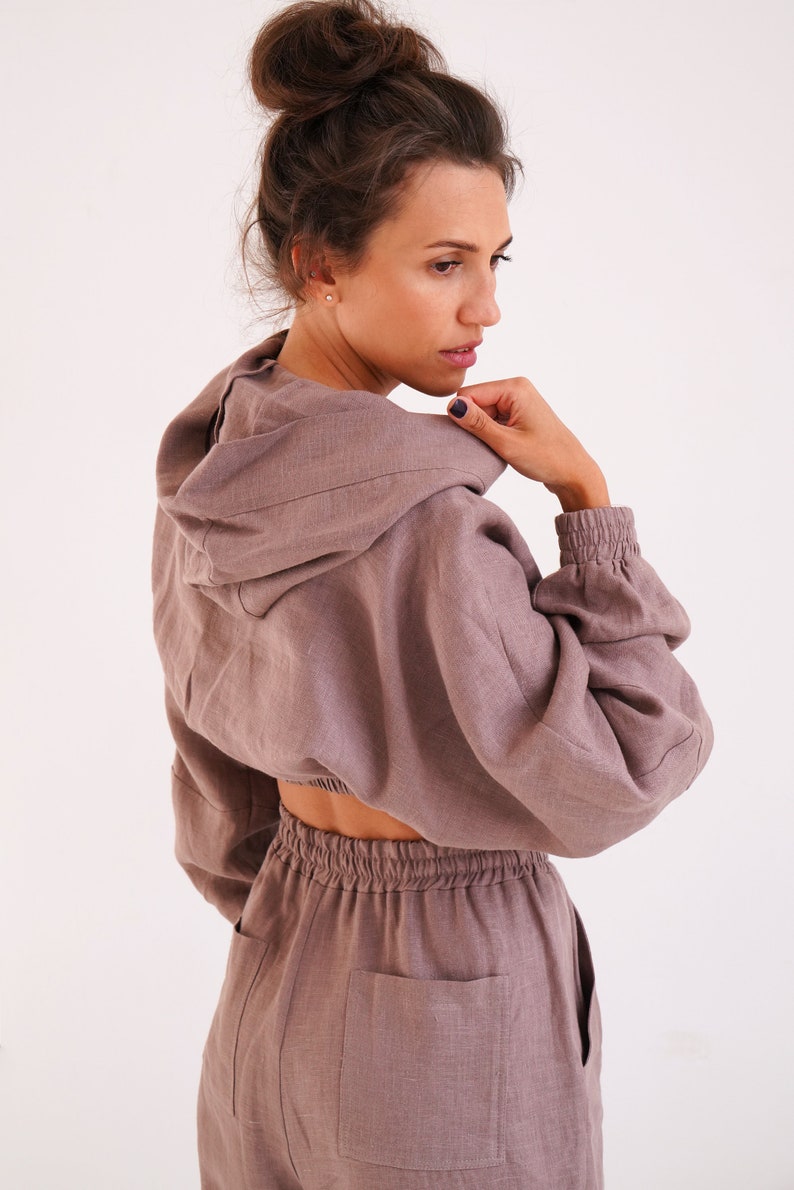 May include: A mauve linen hooded jumpsuit with a cropped top and long pants. The top has a drawstring waist and the pants have a patch pocket on the back.