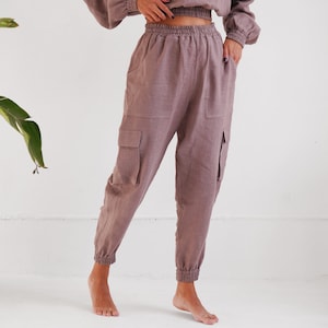 May include: A mauve linen hoodie and matching cargo pants. The hoodie has a drawstring hood and a kangaroo pocket. The pants have a drawstring waistband and two large cargo pockets on the sides.