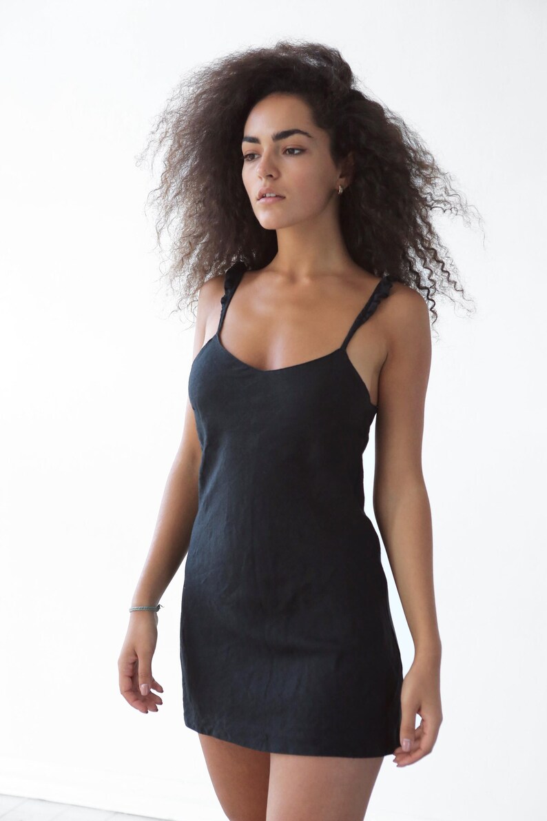 May include: A woman with curly brown hair wearing a black sleeveless dress with a scoop neck.