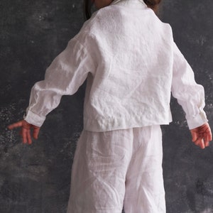 Pu&ograve; includere: Un completo di camicia e pantaloni in lino bianco per un bambino. La camicia ha un colletto classico e maniche lunghe. I pantaloni hanno una vestibilit&agrave; rilassata.