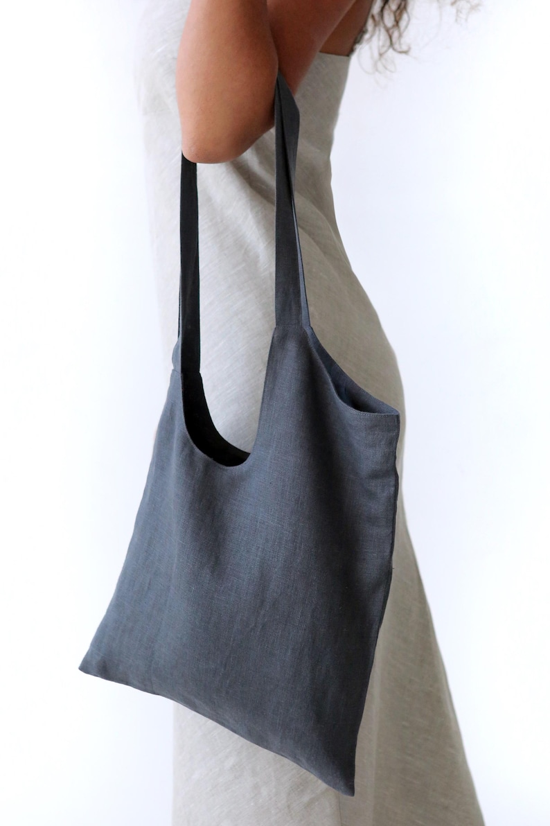 May include: A dark grey linen tote bag with long straps. The bag is large enough to carry groceries or other items.