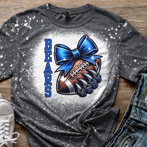May include: A gray t-shirt with a white bleach splatter design. The shirt features a blue and white football with a blue bow and the word "BEARS" in vertical text.