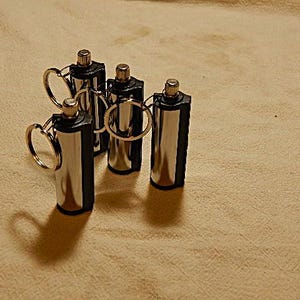 May include: Five silver and black metal fire starters with key rings. The fire starters are cylindrical and have a black plastic cap on one end.