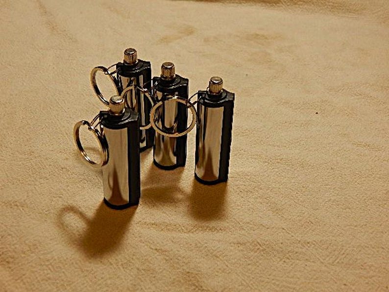 May include: Five silver and black metal fire starters with key rings. The fire starters are cylindrical and have a black plastic cap on one end.