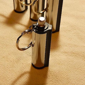 May include: A silver and black metal fire starter with a key ring. The fire starter has a small, round, silver button on the top.
