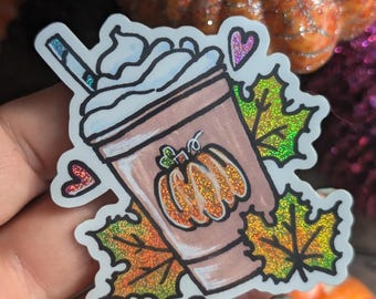 Peut inclure: Un autocollant représentant un latte à la citrouille avec de la crème fouettée et une paille, entouré de feuilles scintillantes et de cœurs. Le latte a un motif de citrouille sur le côté.