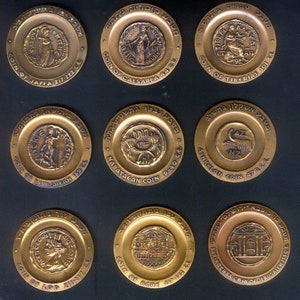 May include: Nine round, gold-colored coins with Hebrew text and dates on each. The coins are arranged in three rows of three. Each coin features a different design, including a person, a building, and a symbol.
