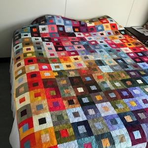 May include: A patchwork quilt featuring a grid of multicoloured fabric squares. Each square contains a smaller, contrasting square in the centre. The quilt displays a wide spectrum of colours including red, orange, yellow, green, blue, and purple.