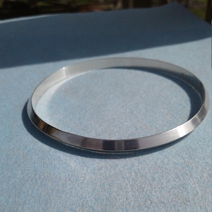 May include: A silver bangle bracelet with a bevelled edge.