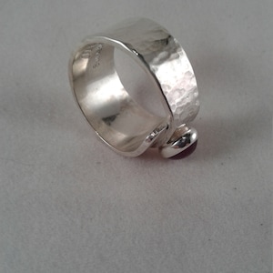 Puede incluir: Un anillo de plata con textura martillada y una peque&ntilde;a piedra preciosa p&uacute;rpura engastada en la banda.
