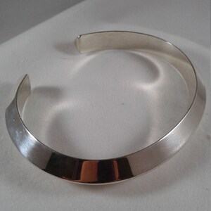 May include: A silver bangle bracelet with a slightly curved, flat design.