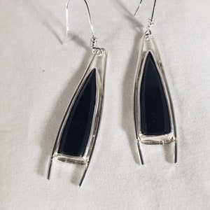 May include: A pair of silver dangle earrings with black gemstone drops. The earrings have a geometric design and are a modern and stylish accessory.