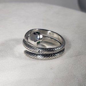 May include: A silver snake ring with green gemstone eyes. The ring is made of two bands that wrap around the finger.