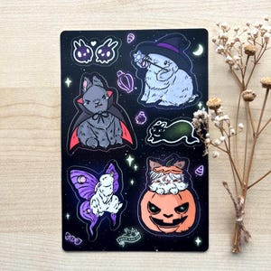 May include: A sheet of black and white stickers featuring cute cartoon bunnies dressed in various Halloween costumes. The stickers include a bunny wearing a witch hat, a bunny wearing a vampire cape, a bunny wearing a pumpkin costume, and a bunny with butterfly wings. The stickers are perfect for adding a touch of whimsy to your Halloween decorations.