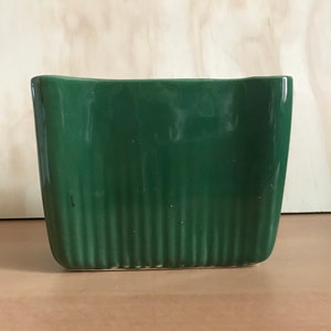 Peut inclure: Un pot de fleurs rectangulaire en céramique vert foncé avec des détails côtelés verticaux. Le pot a un bord supérieur légèrement incurvé et une base plate, adapté à l'intérieur ou à l'extérieur.