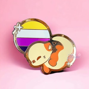 May include: Gold-tone enamel pin featuring a cartoon animal curled up with a heart-shaped background. The heart is divided into four stripes of yellow, white, purple, and black, representing the non-binary pride flag.