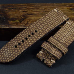 Op de afbeelding: Een bruin leren horlogebandje met een textuurpatroon. Het bandje is gestikt langs de randen en is ontworpen voor een horloge met veerpennen.