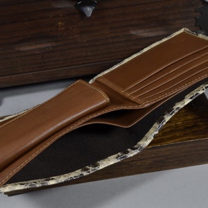 May include: A brown leather wallet with multiple card slots and a billfold. The wallet is open and the interior is lined with a black fabric. The exterior of the wallet is made of a snakeskin pattern.