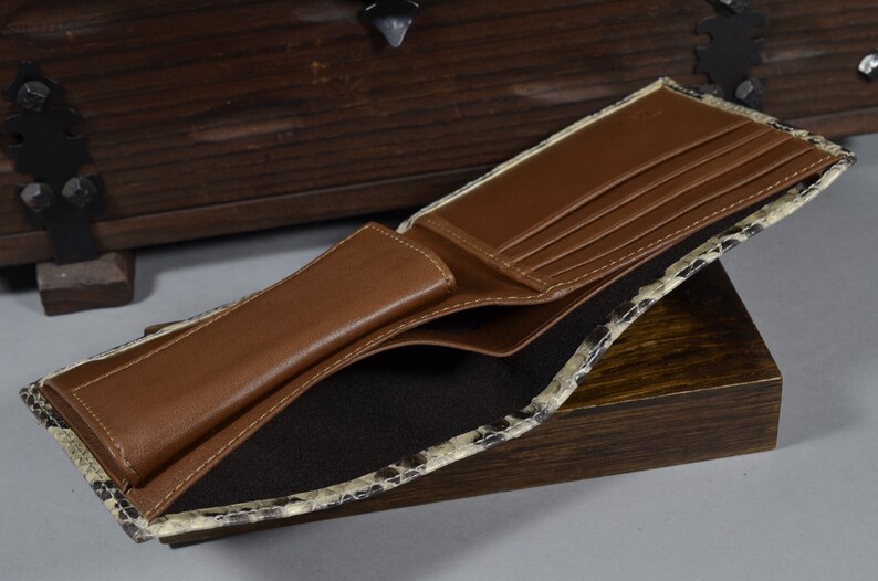 May include: A brown leather wallet with multiple card slots and a billfold. The wallet is open and the interior is lined with a black fabric. The exterior of the wallet is made of a snakeskin pattern.