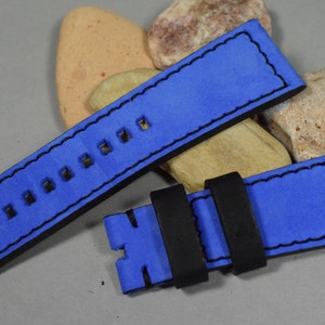 Op de afbeelding: Een blauw leren horlogebandje met zwarte stiksels en een zwarte gesp. Het bandje heeft meerdere gaten om de maat aan te passen.
