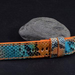 Może przedstawiać: Pasek do zegarka wykonany ze skóry węża w kolorze niebieskim, brązowym i szarym ze szwami w kolorze pomarańczowym. Pasek jest przeznaczony do zegarka ze standardową szerokością uszek.