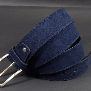 May include: A dark blue suede belt with a silver buckle. The belt is folded in half and the buckle is visible.