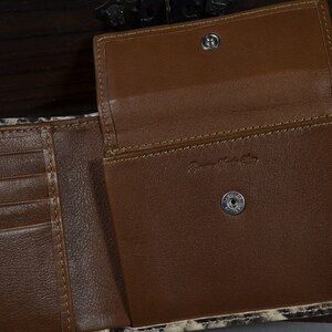 May include: A brown leather wallet with a snakeskin pattern on the outside. The wallet is open to reveal multiple card slots and a billfold. The wallet has a brown leather interior and two metal snaps.