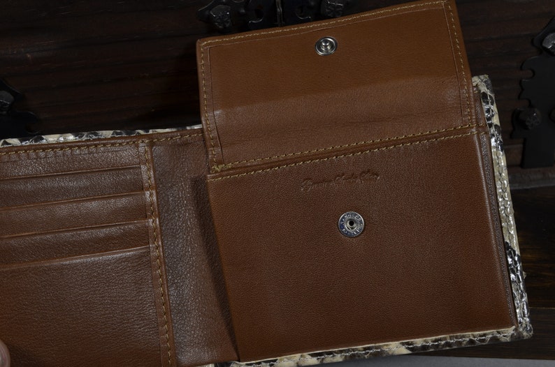 May include: A brown leather wallet with a snakeskin pattern on the outside. The wallet is open to reveal multiple card slots and a billfold. The wallet has a brown leather interior and two metal snaps.