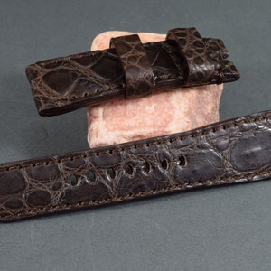 Op de afbeelding: Een donkerbruin alligator horlogebandje met een gestikte rand en een gesp. Het bandje is gemaakt van echt alligatorleer en is ontworpen voor een horloge met een lugbreedte van 22 mm.