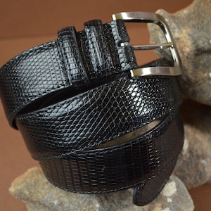 May include: A black leather belt with a silver buckle. The belt is made of a textured material that resembles snakeskin.