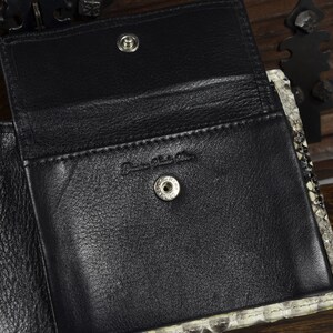 May include: A black leather wallet with a snakeskin pattern on the exterior. The wallet is open to reveal a black leather interior with multiple card slots and a snap closure.