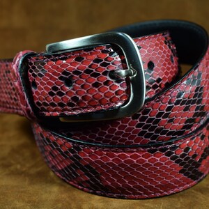 May include: A red and black snakeskin belt with a silver buckle. The belt is made of genuine leather and has a classic design.