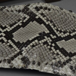 May include: A close-up of a white and black snakeskin wallet. The wallet is made of genuine leather and has a textured surface.