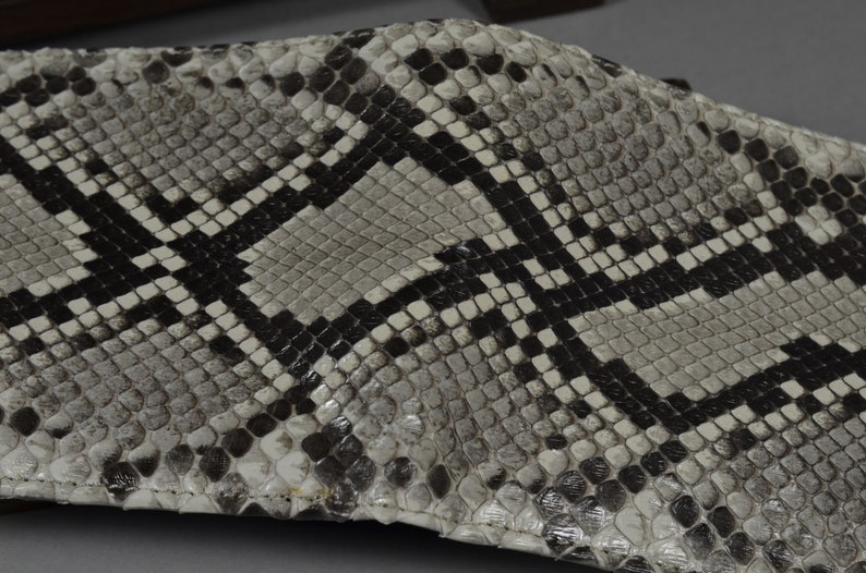 May include: A close-up of a white and black snakeskin wallet. The wallet is made of genuine leather and has a textured surface.