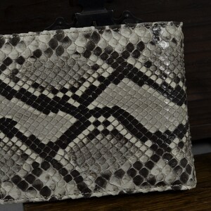 Pode incluir: Uma carteira de pele de cobra branca e preta com um padr&atilde;o de diamante.