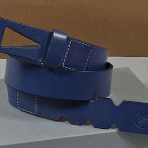 May include: A blue leather belt with a unique buckle design. The belt is folded in half and has a stitched edge.