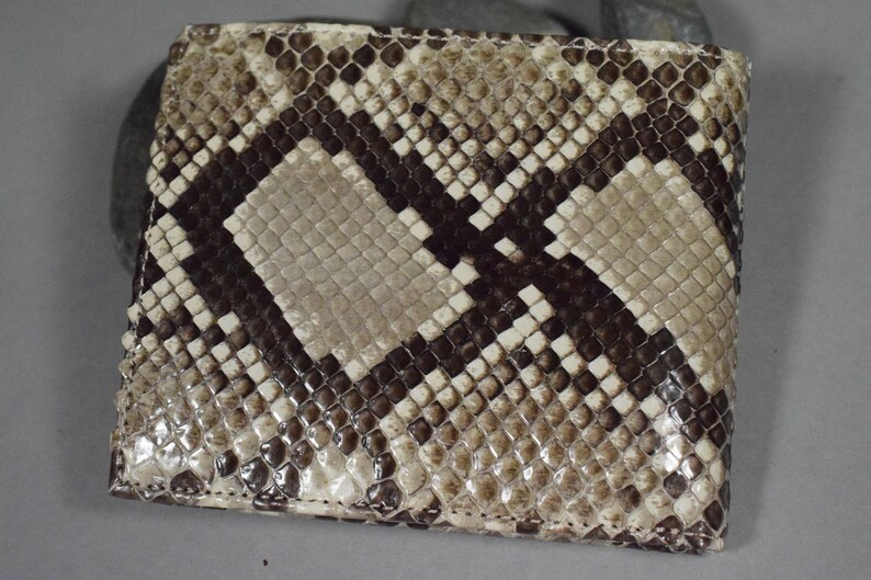 K&ouml;nnte beinhalten: Eine braune und wei&szlig;e Schlangenleder-Geldb&ouml;rse mit einem Rautenmuster. Die Geldb&ouml;rse ist aus echtem Leder gefertigt und hat eine glatte Oberfl&auml;che.