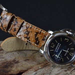 Puede incluir: Una correa de reloj de cuero marrón con un patrón blanco y negro. La correa está unida a un reloj plateado con una esfera negra y marcas blancas. La esfera del reloj dice "Luminor Marina" y "Panerai".